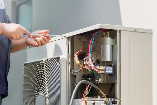 A technician is carefully using a screwdriver to repair an outdoor air conditioning unit with exposed wiring, demonstrating the same precision you'd expect in furnace repair.